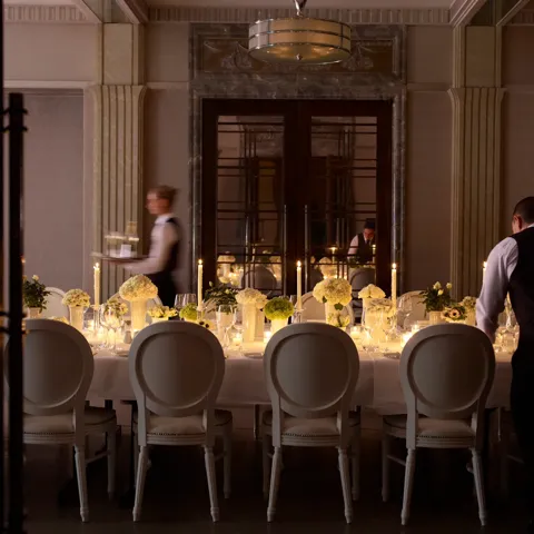 Elegant private dining room with a long candlelit table, floral centrepieces, and staff preparing place settings.