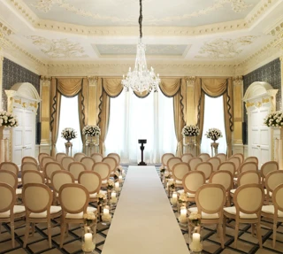 Elegant ballroom set for a wedding ceremony with cream chairs, floral arrangements, candlelit aisle, and a crystal chandelier