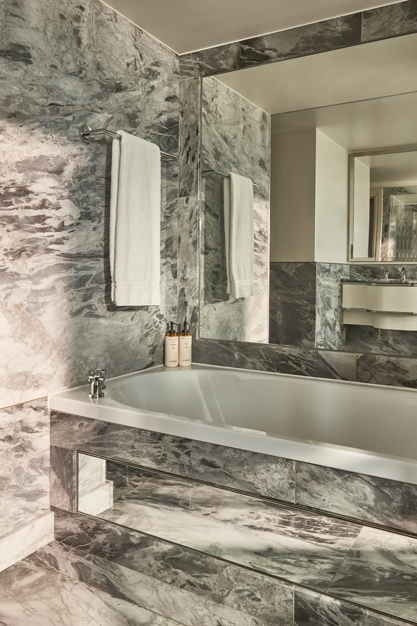 Luxurious marble bathroom with deep bathtub, mirrored walls, and mounted white towels