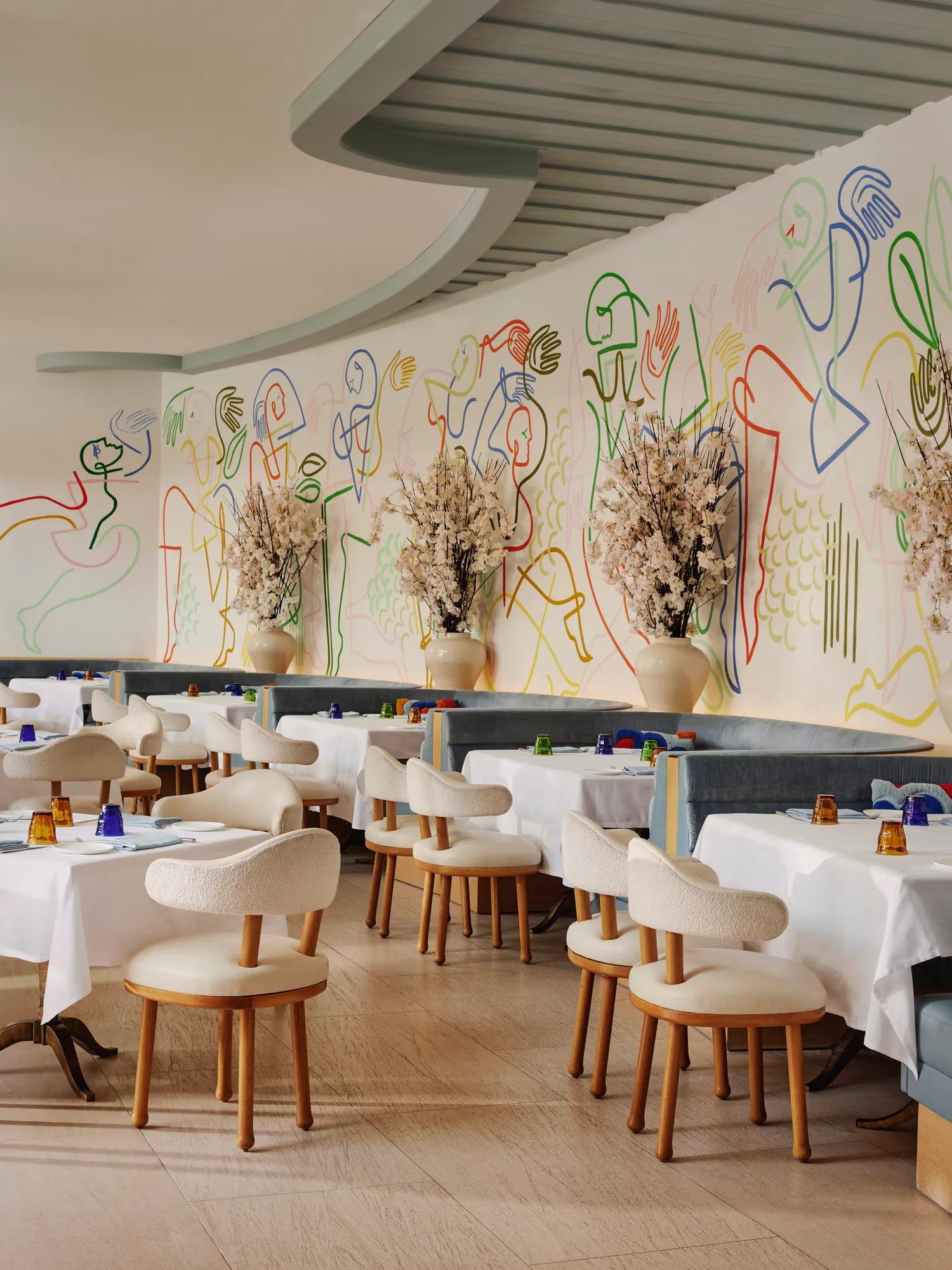 Rows of white-clothed tables and cream chairs beneath a wavy ceiling and vibrant mural at The Terrace.