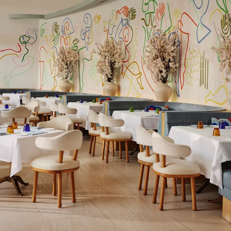 Rows of white-clothed tables and cream chairs beneath a wavy ceiling and vibrant mural at The Terrace.