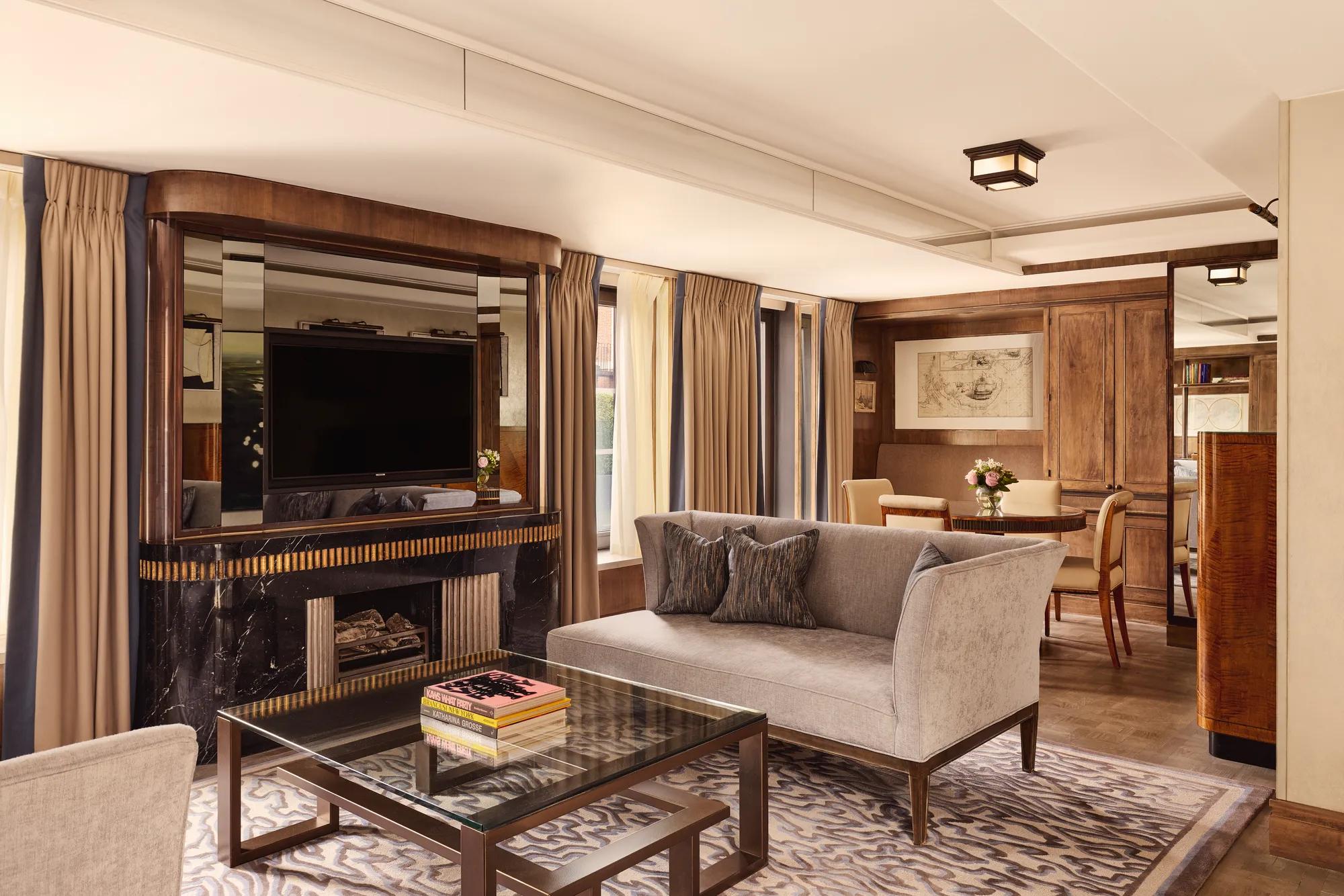 Elegant suite with grey sofa, marble fireplace, mirrored TV wall, and dining area in warm wood tones.