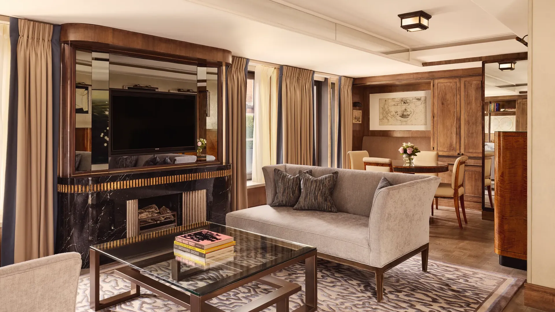 Elegant suite with grey sofa, marble fireplace, mirrored TV wall, and dining area in warm wood tones.