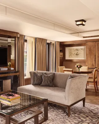 Elegant suite with grey sofa, marble fireplace, mirrored TV wall, and dining area in warm wood tones.