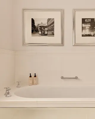 Cream bathroom with freestanding bathtub, chrome taps, toiletries, and two framed black-and-white photos above.