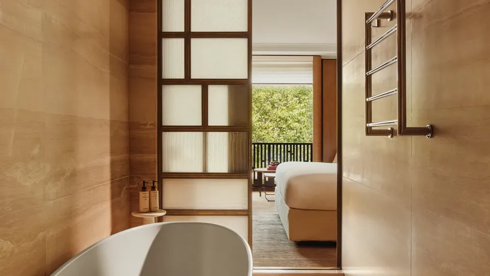 Freestanding oval bathtub in a wood-panelled bathroom, with sliding screen opening to a bedroom and balcony views.