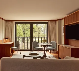 Contemporary suite living space with pale wood floors, a desk, round dining table with blue chairs, and large windows opening onto views of Hyde Park.