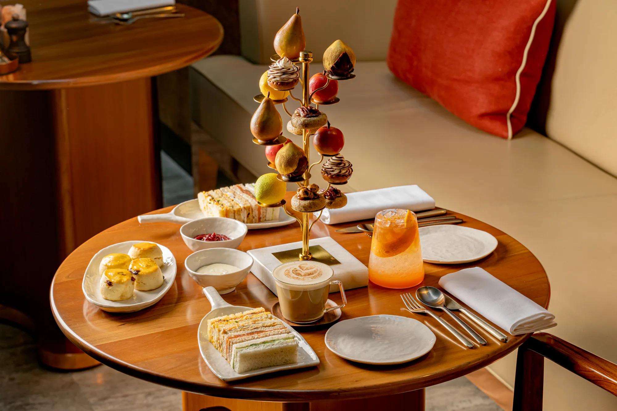Afternoon tea selection with sandwiches, pastries, fruit desserts and drinks served on a table in a luxury lounge setting.