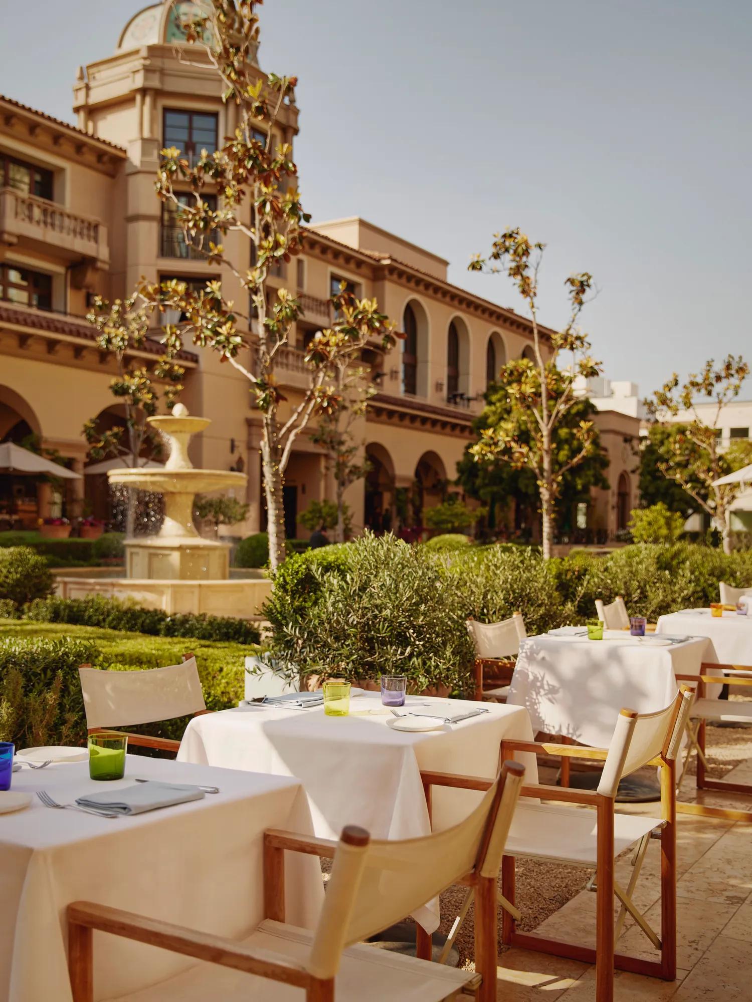 The Terrace tables with white umbrellas by a fountain, with a domed tower in the landscaped courtyard.