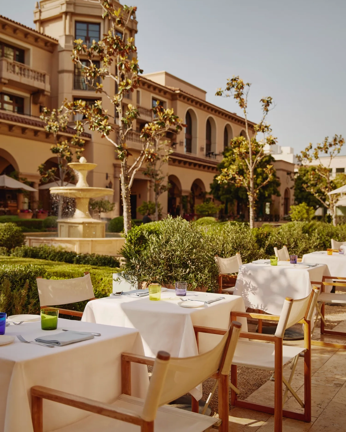 The Terrace tables with white umbrellas by a fountain, with a domed tower in the landscaped courtyard.