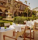 The Terrace tables with white umbrellas by a fountain, with a domed tower in the landscaped courtyard.