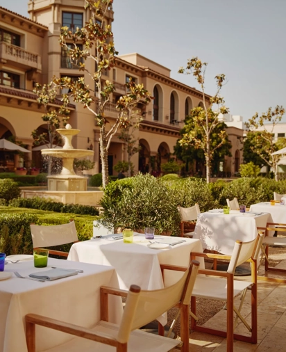 The Terrace tables with white umbrellas by a fountain, with a domed tower in the landscaped courtyard.