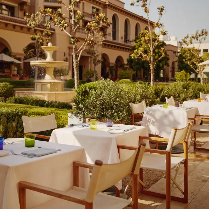 The Terrace tables with white umbrellas by a fountain, with a domed tower in the landscaped courtyard.