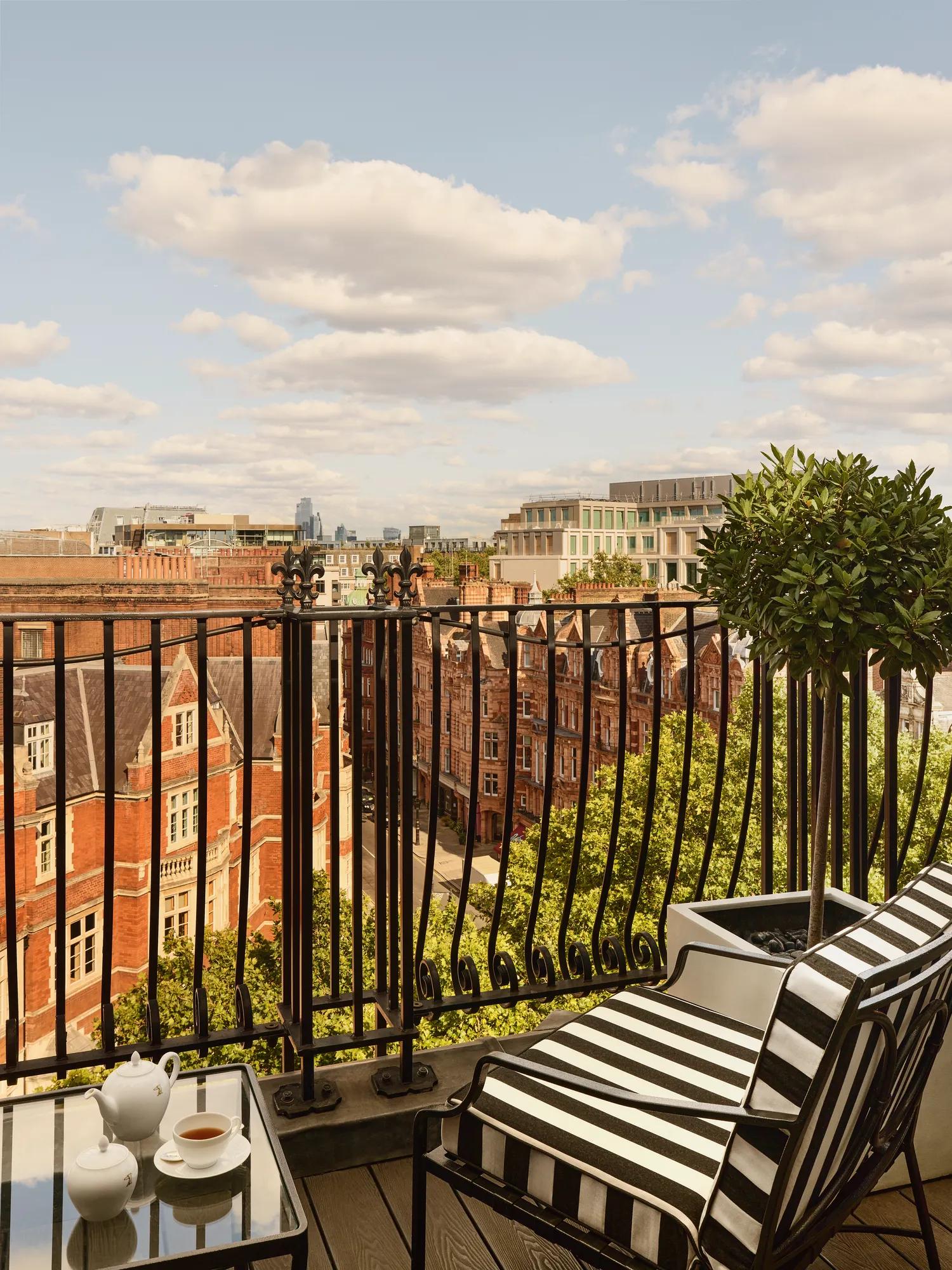 Private balcony with striped chair overlooking London rooftops and city skyline under blue sky.
