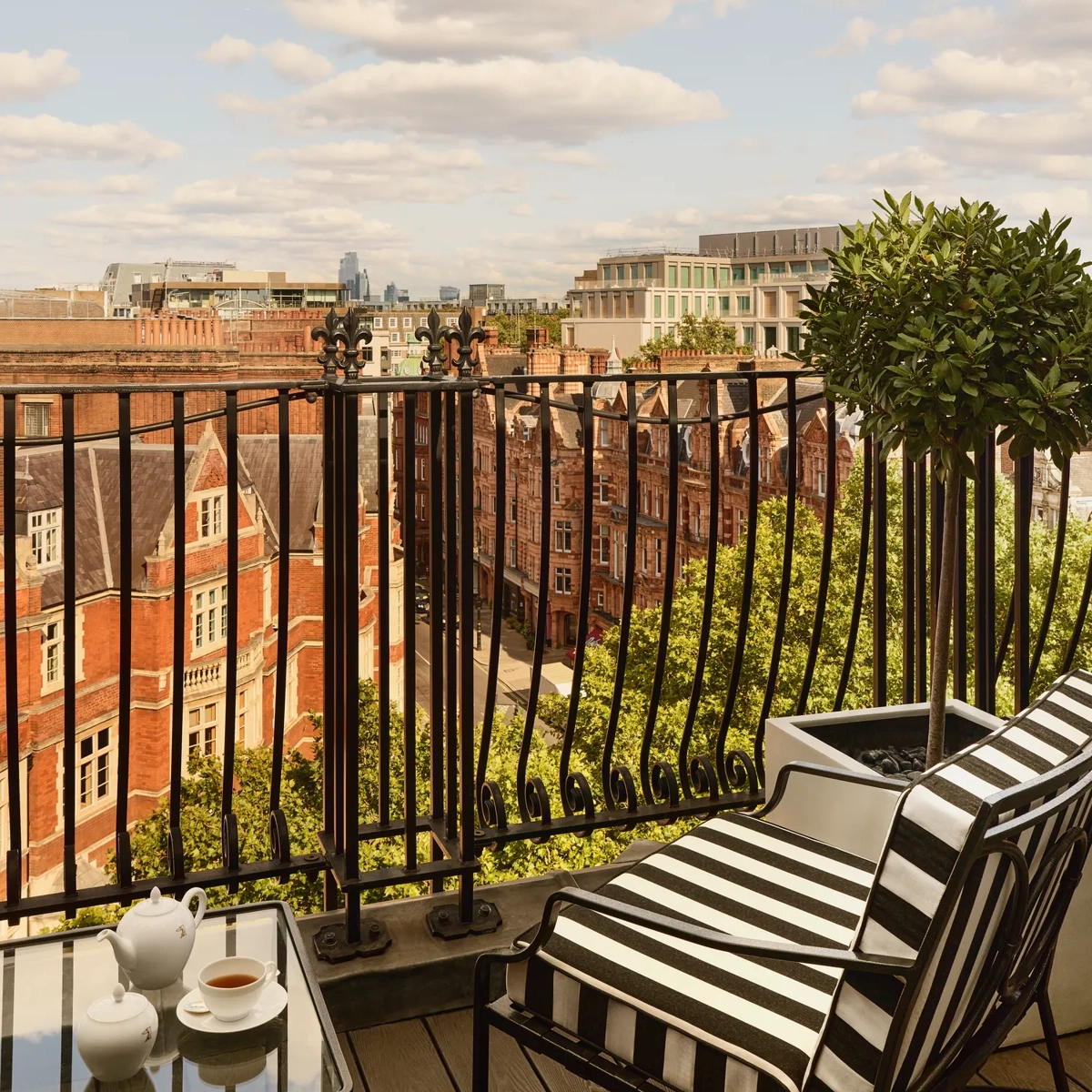 Private balcony with striped chair overlooking London rooftops and city skyline under blue sky.