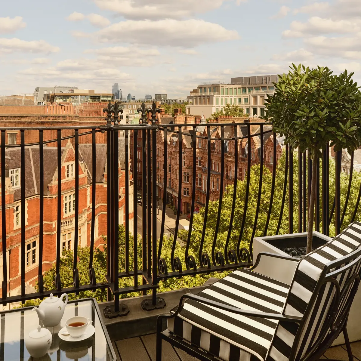 Private balcony with striped chair overlooking London rooftops and city skyline under blue sky.