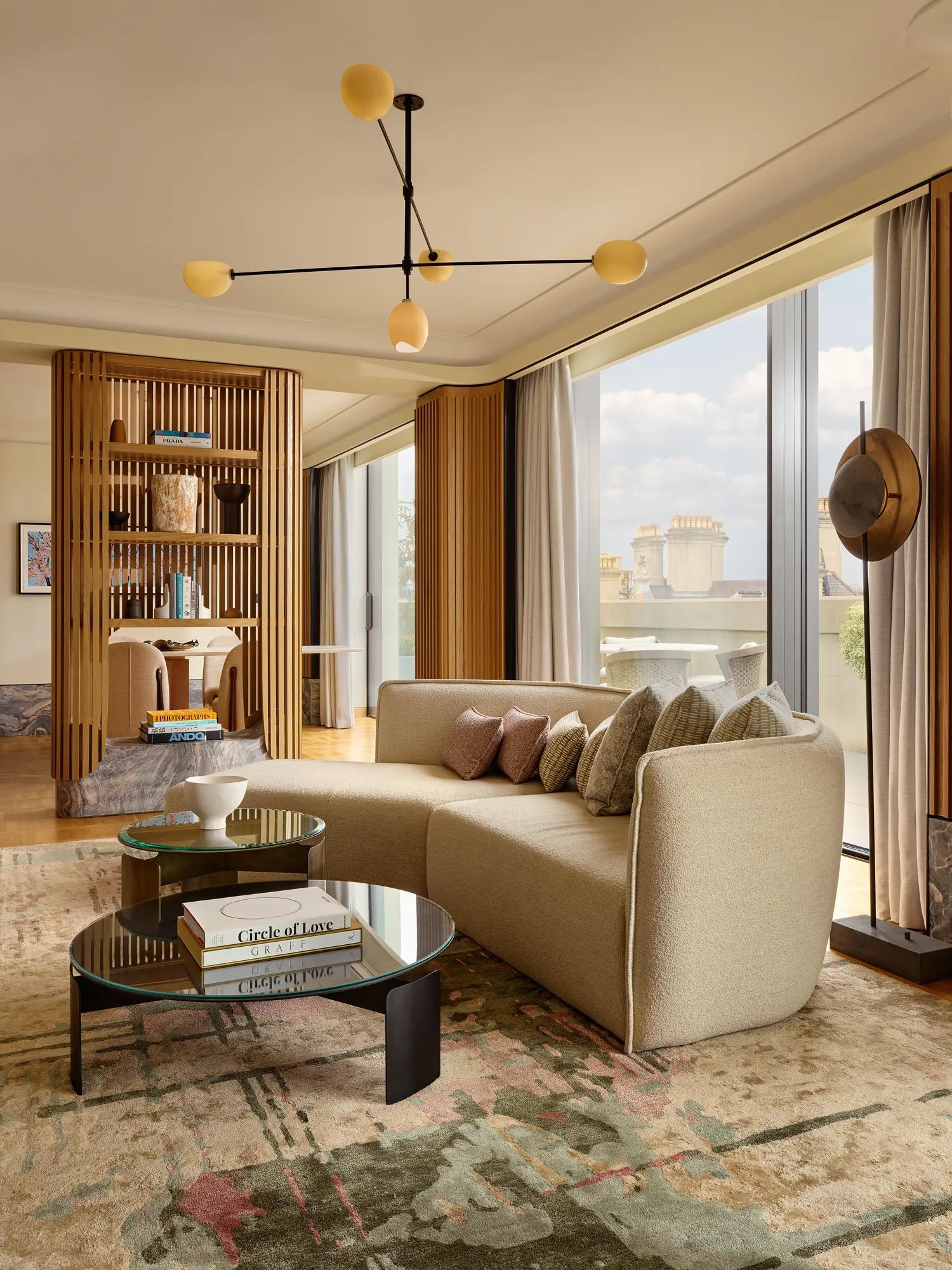 Living area with a curved cream sofa, round glass coffee tables, and floor-to-ceiling windows opening to the terrace.