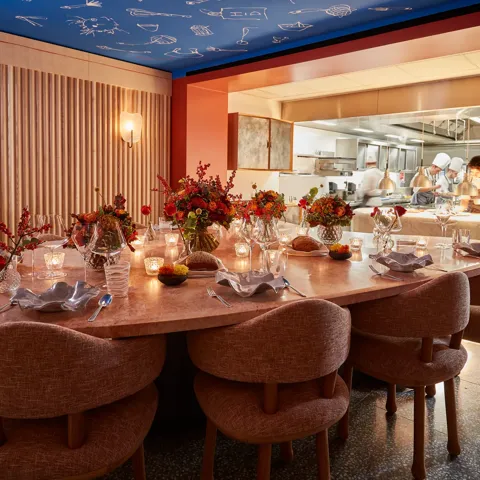 Private dining table set with candles and flowers beside an open kitchen, where chefs prepare dishes behind a glass partition.