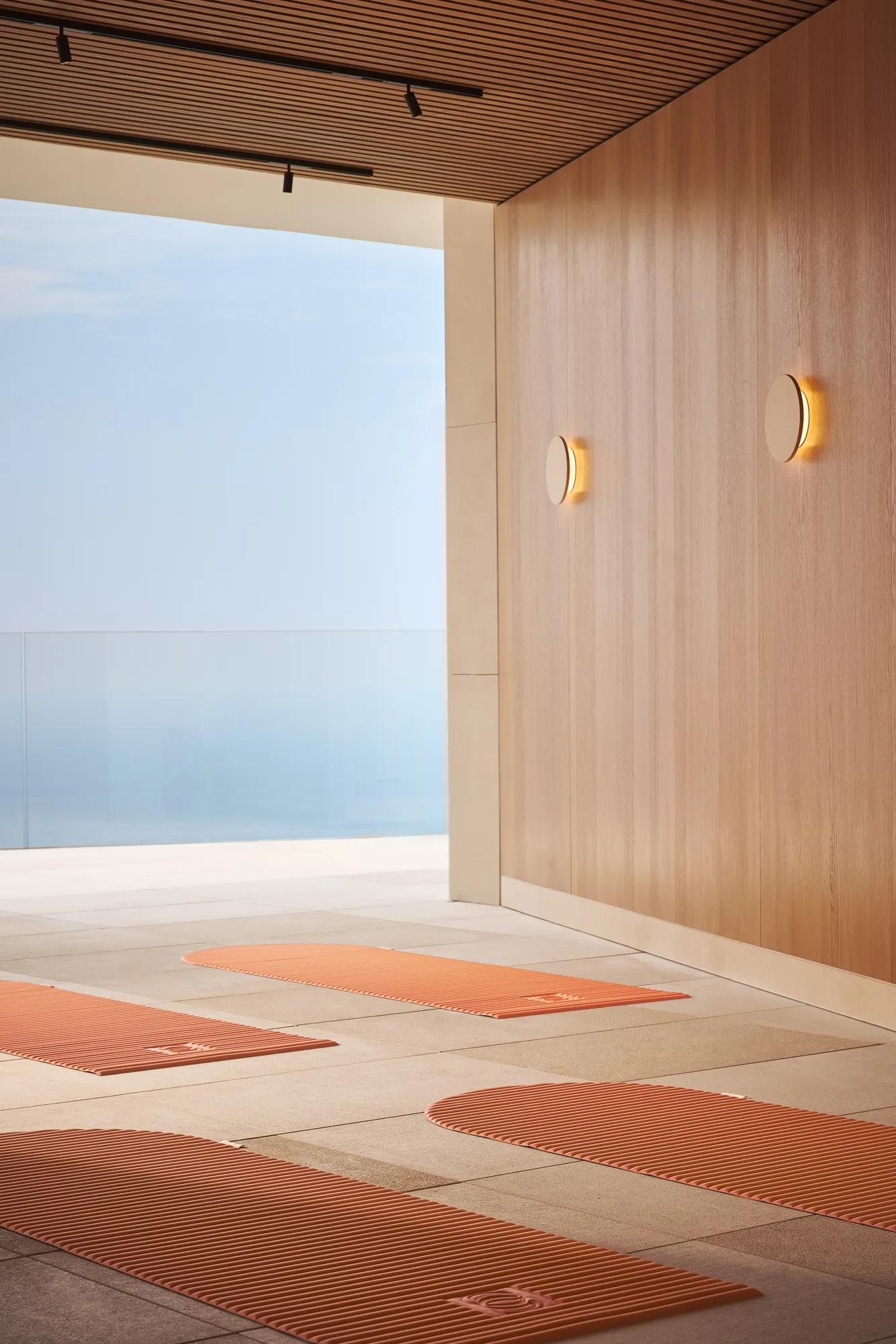 Yoga mats laid out in a serene indoor-outdoor space with sea views beyond a glass railing.