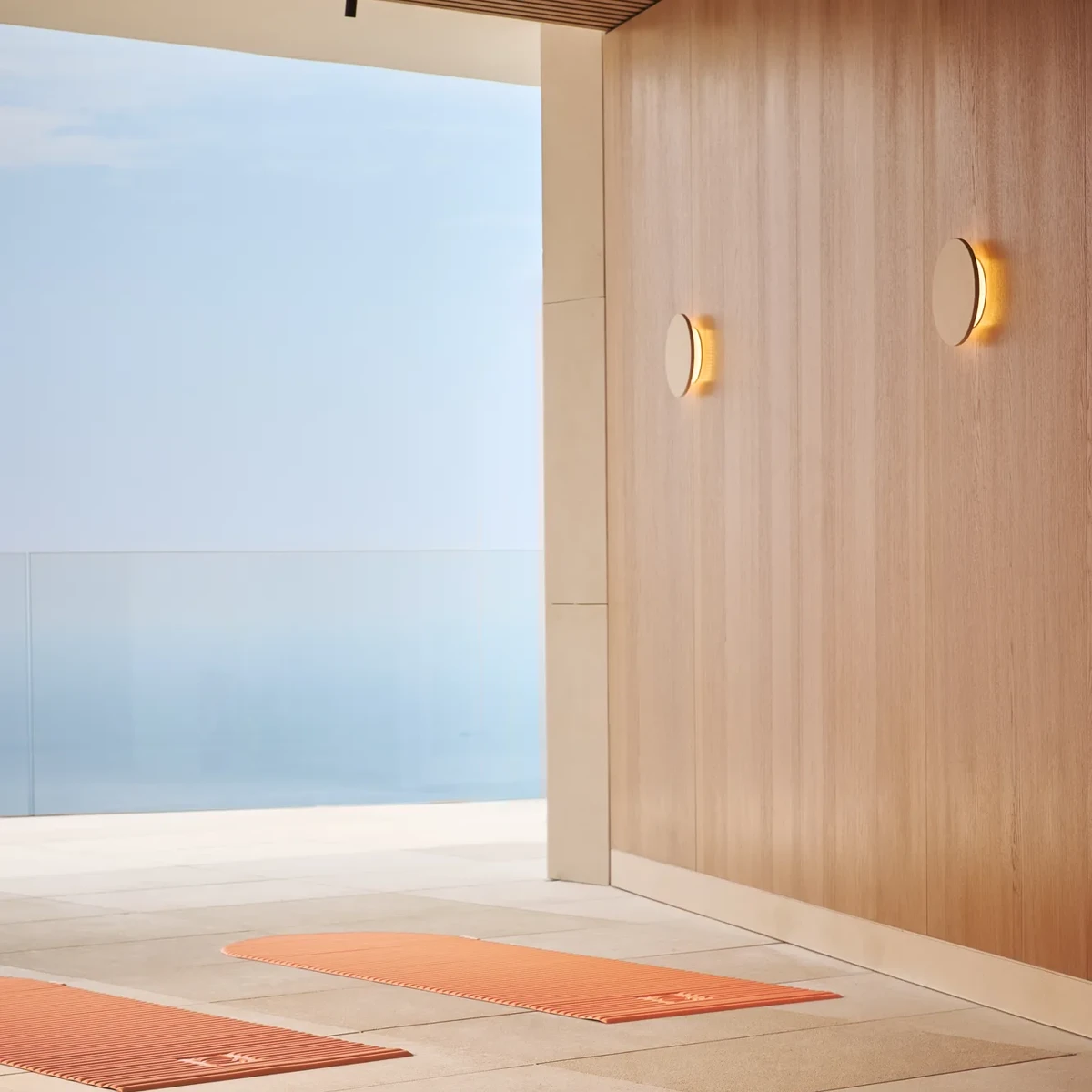 Yoga mats laid out in a serene indoor-outdoor space with sea views beyond a glass railing.