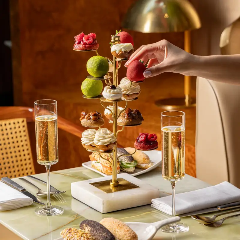Luxurious afternoon tea with mini pastries and sandwiches served on sculptural stand with champagne flutes.