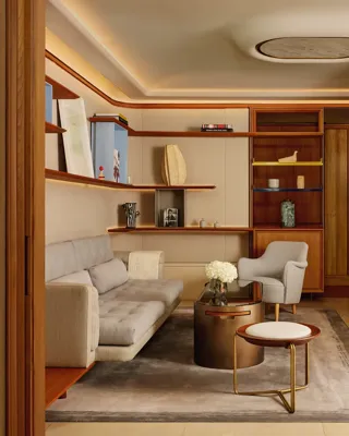 A stylish sitting room with a pale grey sofa, armchair, and round coffee table, framed by wooden shelving displaying books and decorative pieces