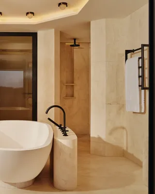 Freestanding oval bathtub in beige marble bathroom with rainfall shower and soft lighting.