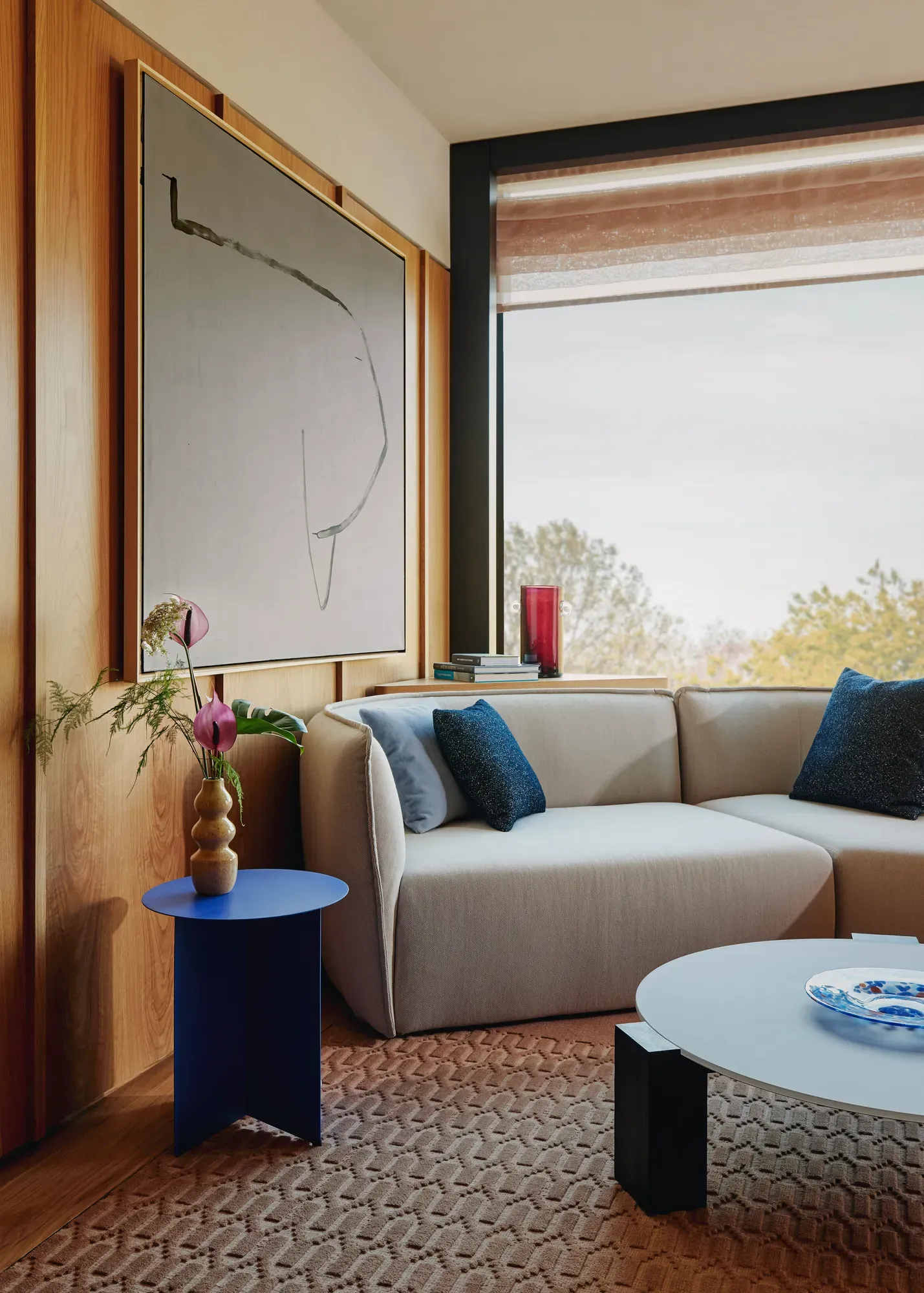 Modern sitting area with a cream corner sofa, abstract wall art, and a blue side table beside a window.