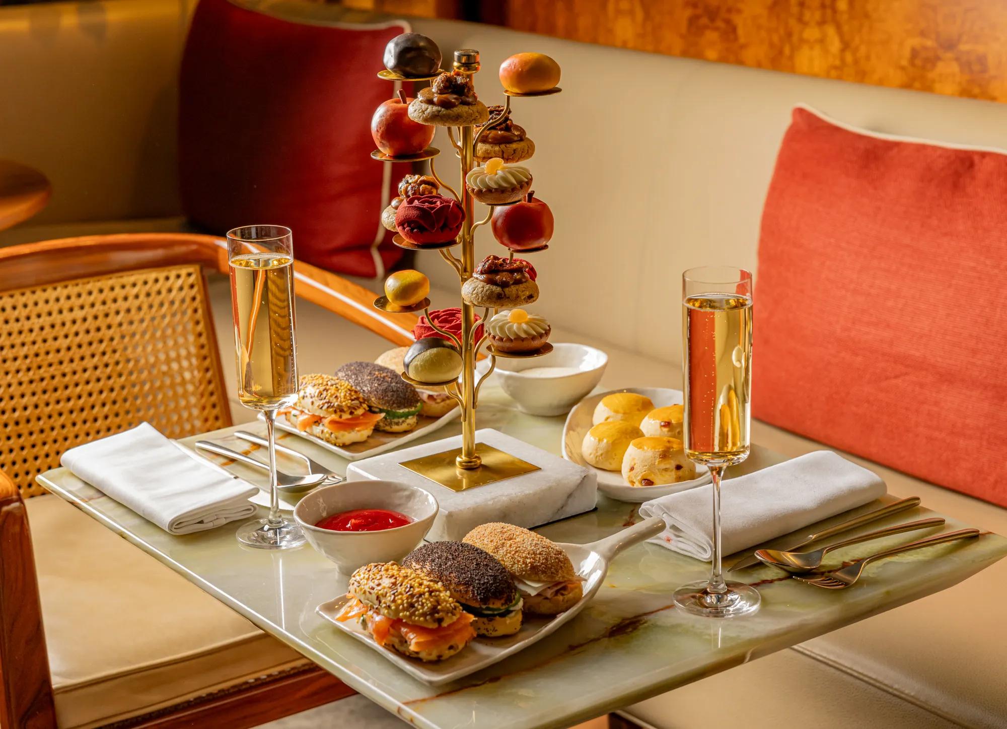 Tiered stand of pastries and savoury bites with champagne flutes on a marble table in a warm, elegant lounge setting.