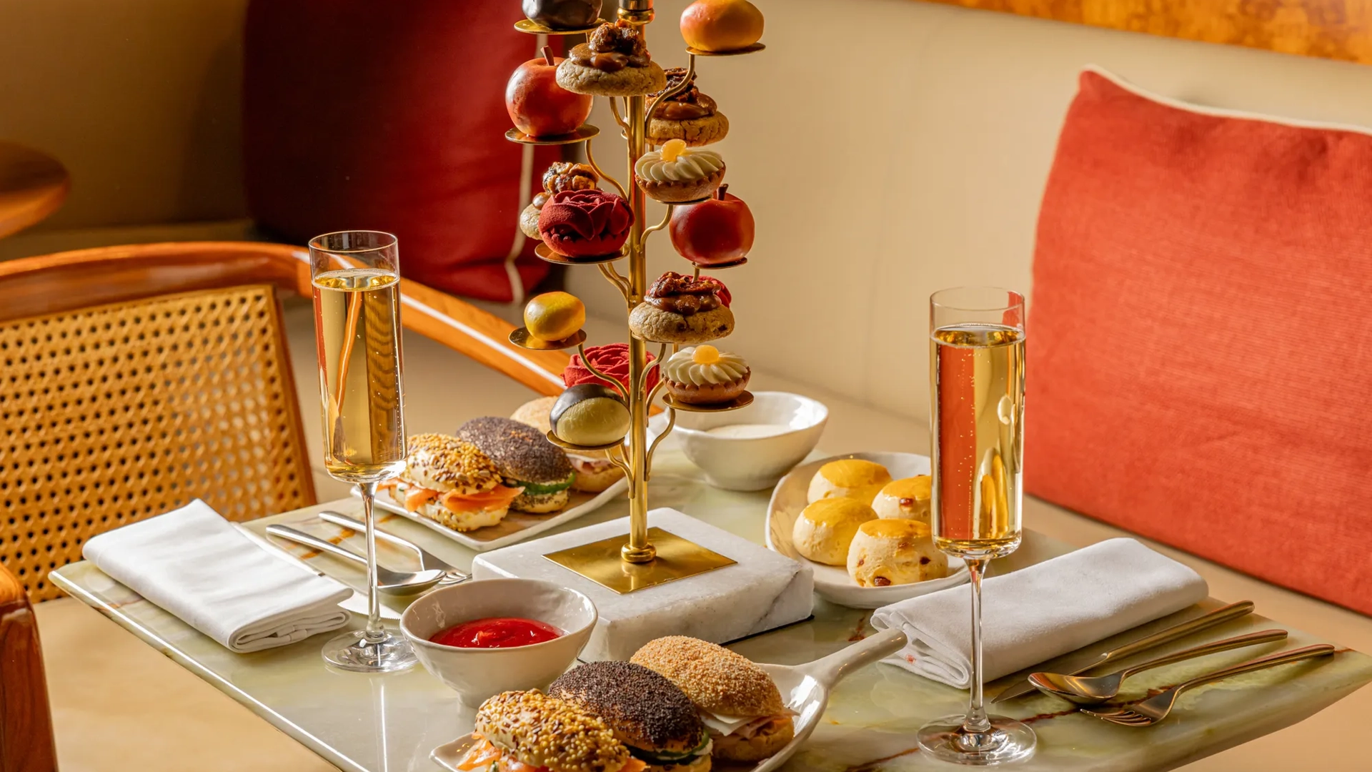 Tiered stand of pastries and savoury bites with champagne flutes on a marble table in a warm, elegant lounge setting.