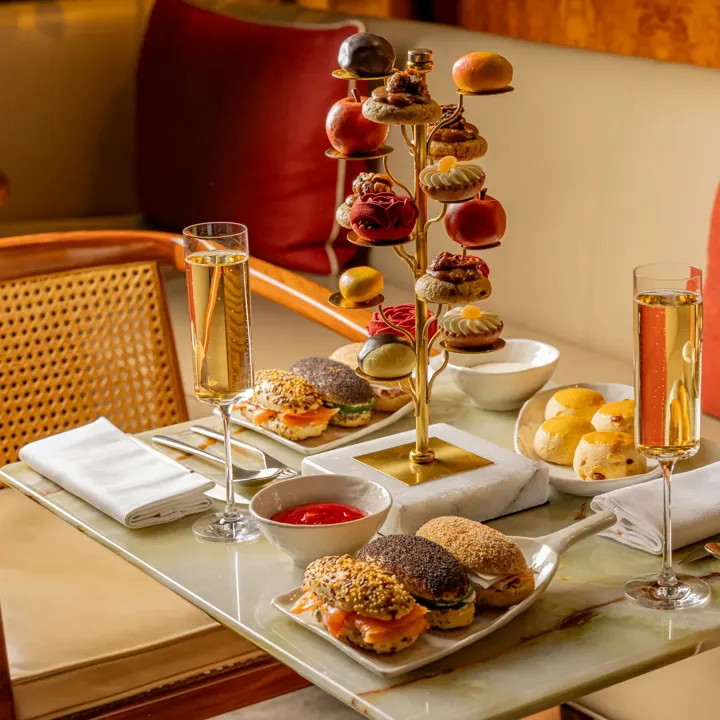 Tiered stand of pastries and savoury bites with champagne flutes on a marble table in a warm, elegant lounge setting.