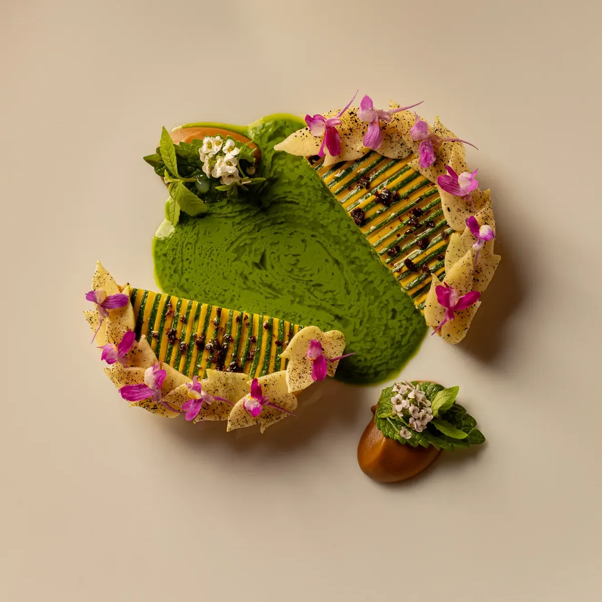 Artfully plated dish with green sauce, layered vegetable slices, and small edible flowers on a white plate.