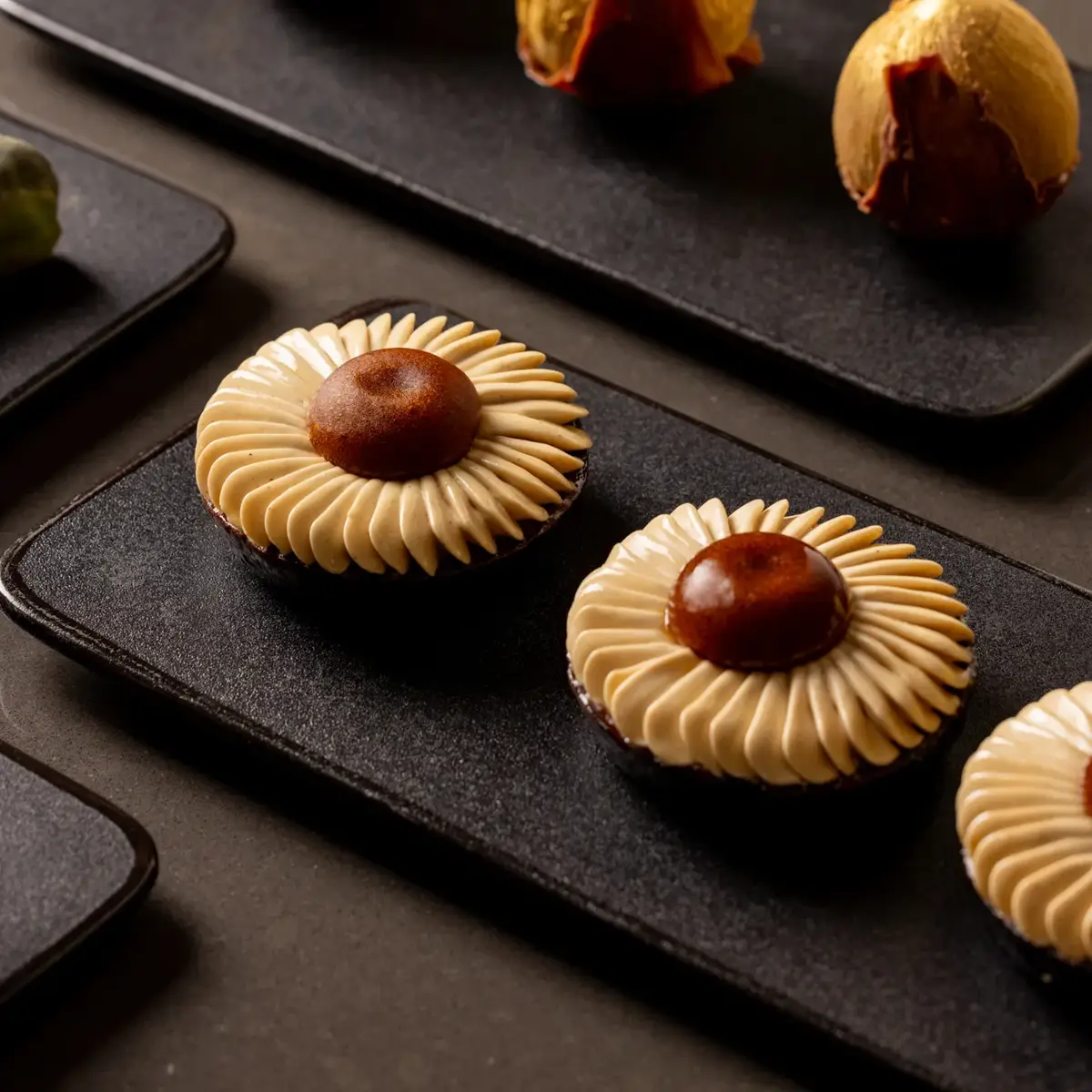 Assorted pastries arranged on black plates, featuring piped cream tarts and fruit-filled desserts.