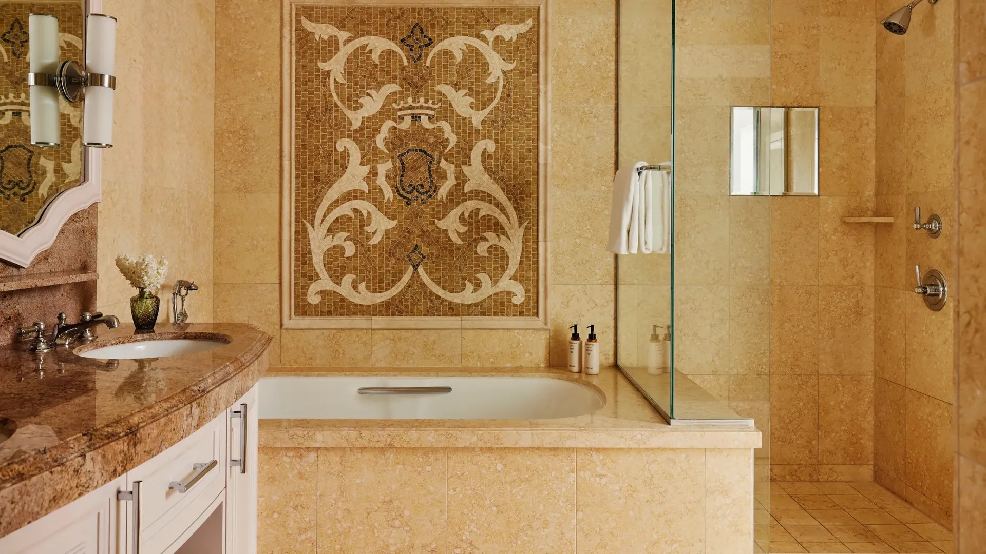 Stone-tiled bathroom with bathtub under an ornate mosaic panel beside a walk-in shower behind a glass screen.