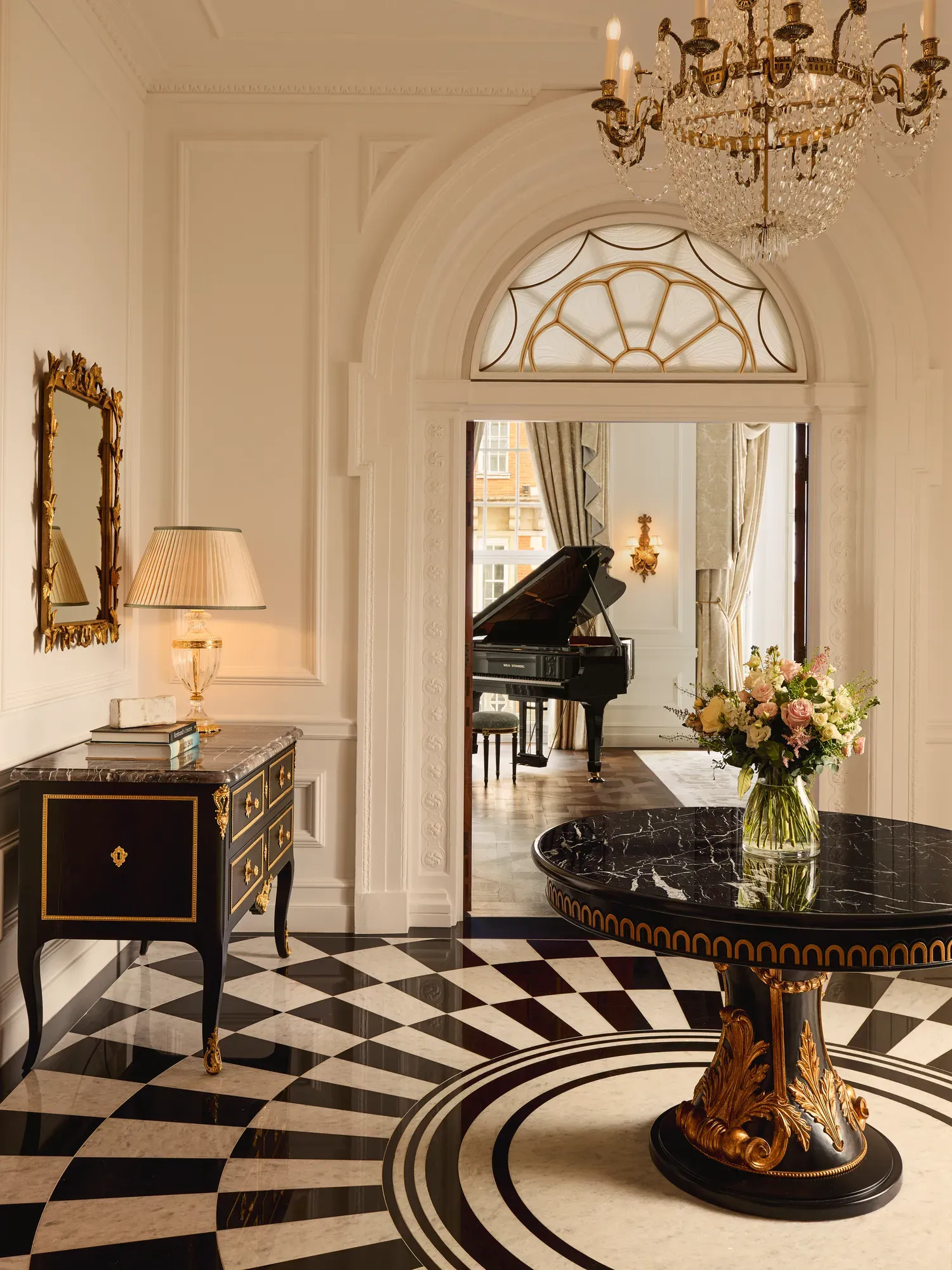 Elegant suite entrance at Claridge’s with a black marble table, chandelier, and view into a room with a grand piano.