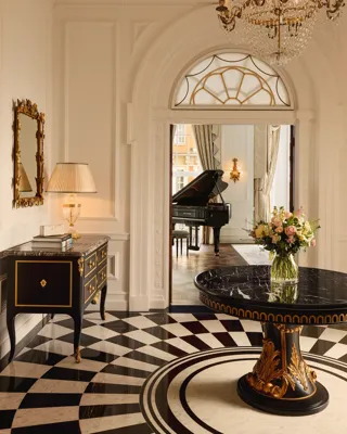Elegant suite entrance at Claridge’s with a black marble table, chandelier, and view into a room with a grand piano.