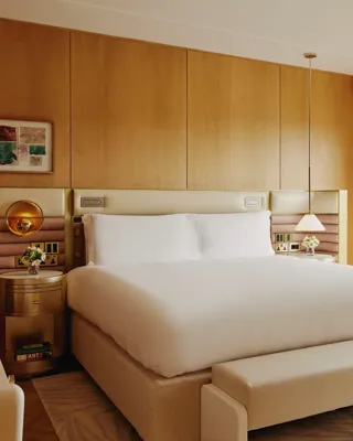 Hotel bedroom with king bed, upholstered headboard, wood-panelled walls, bedside lighting and large window with treetop views.