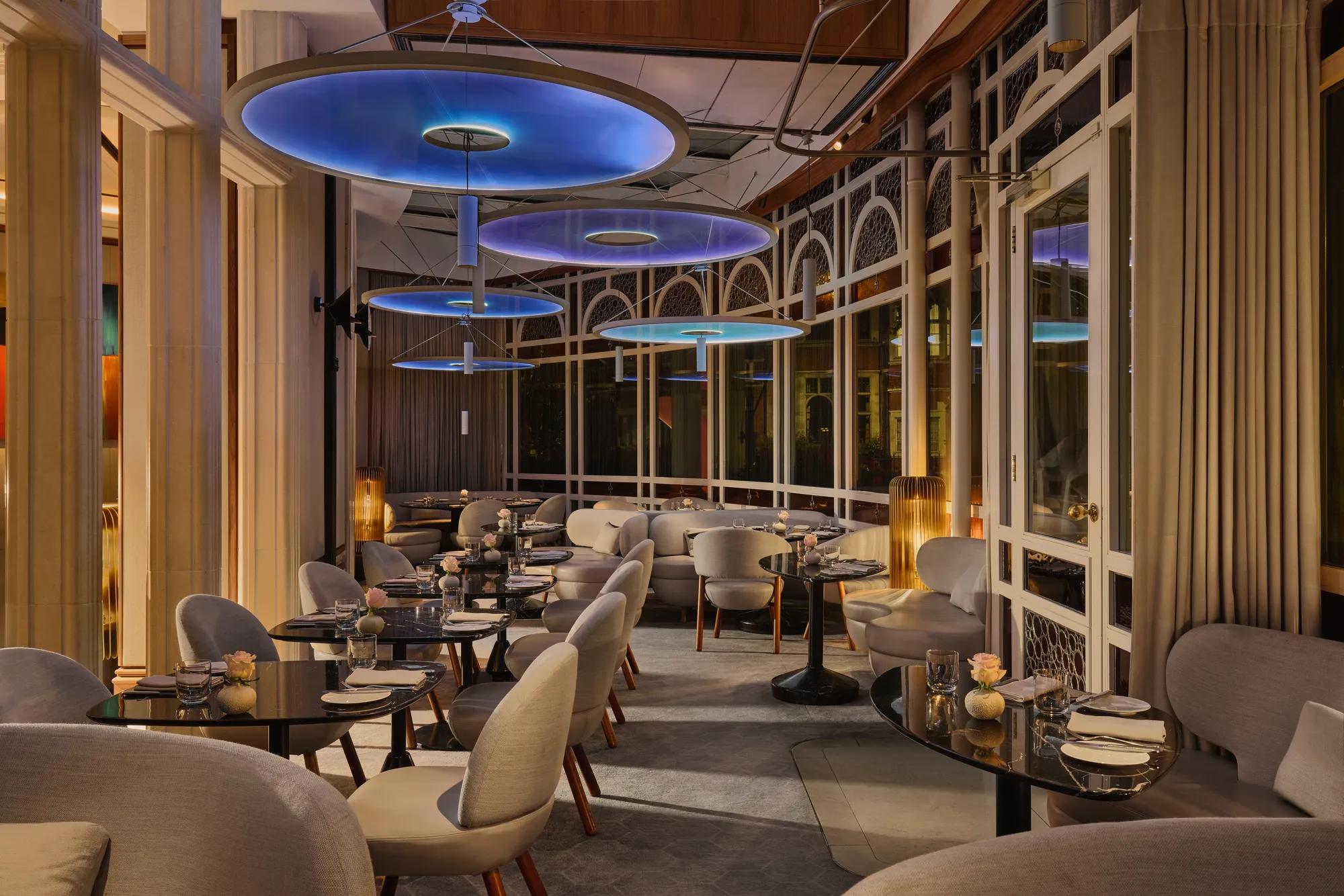 Elegant restaurant dining room with curved seating, dark tables, and large blue circular ceiling lights.