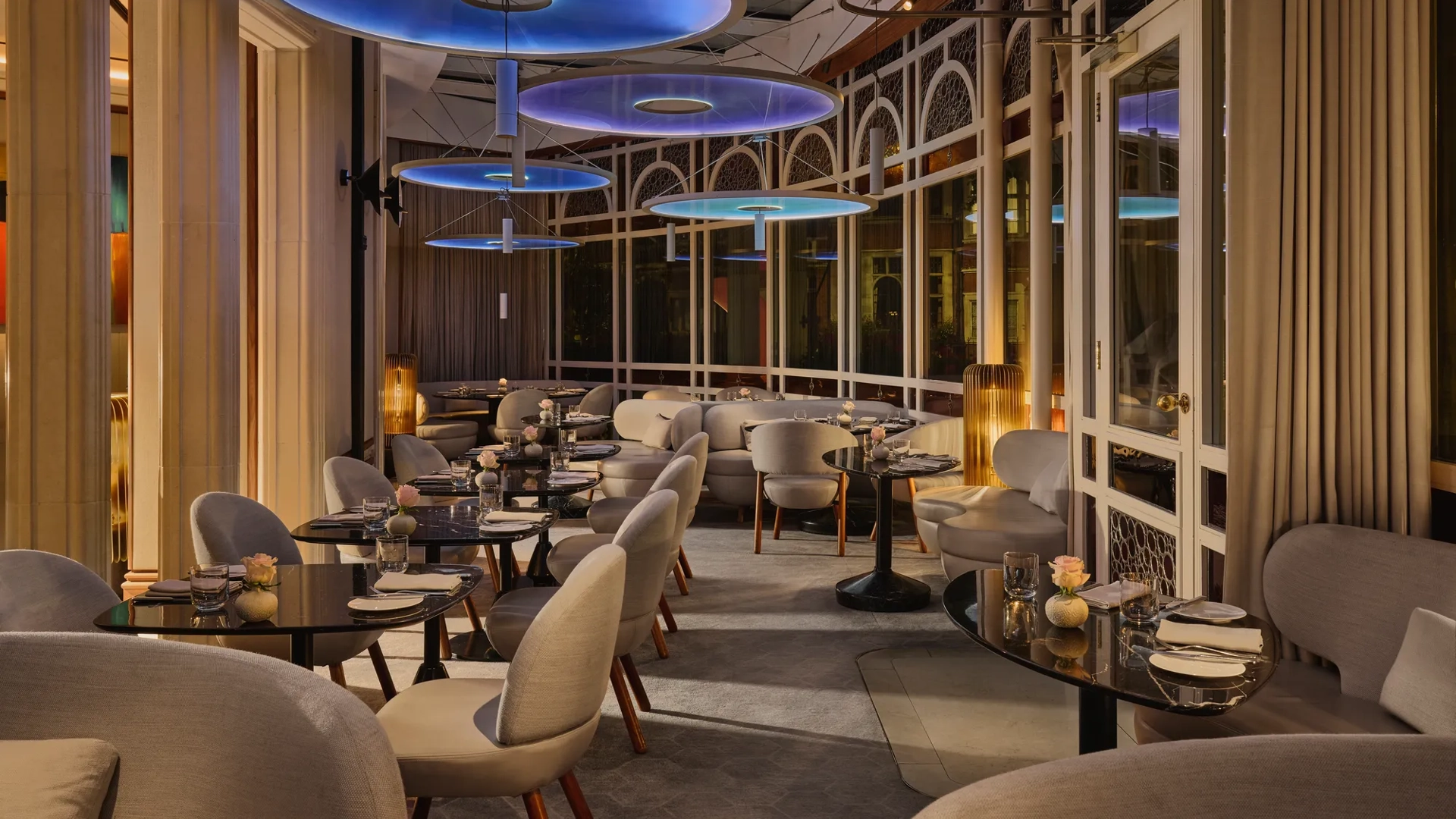 Elegant restaurant dining room with curved seating, dark tables, and large blue circular ceiling lights.