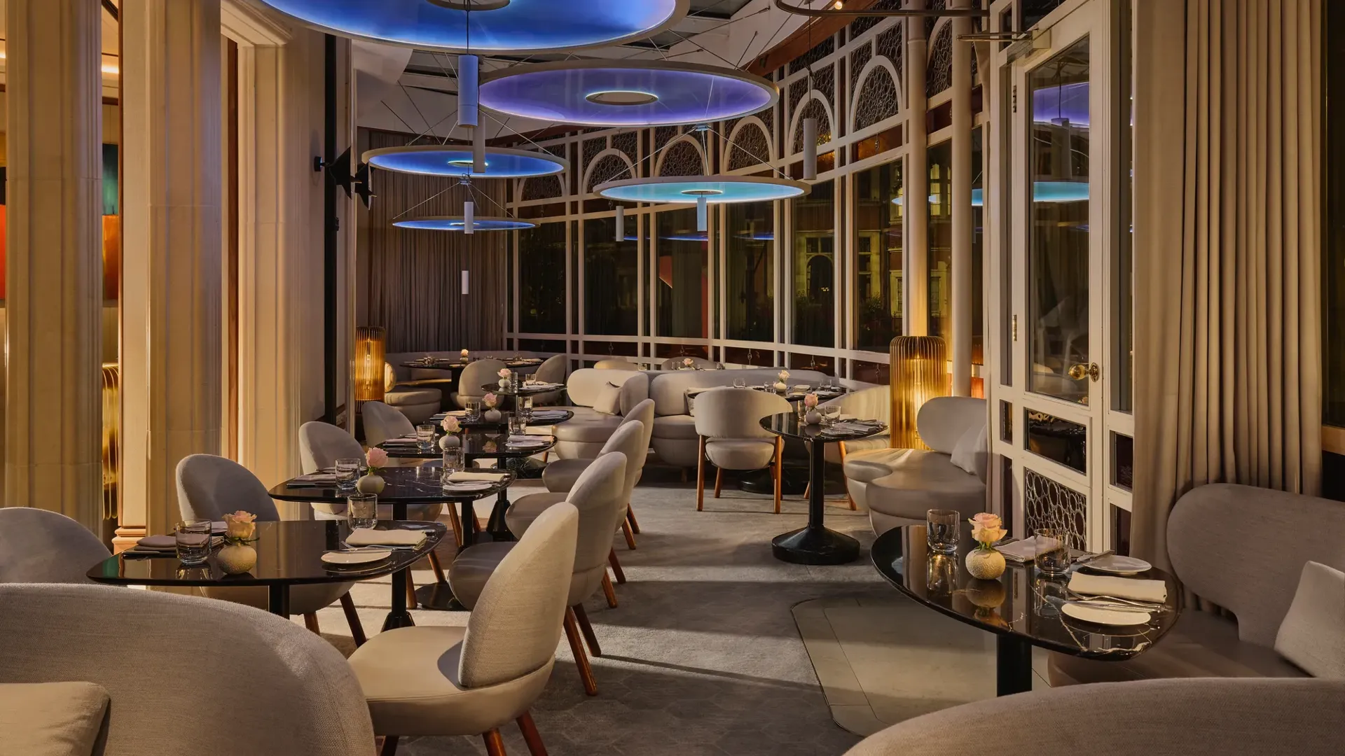 Elegant restaurant dining room with curved seating, dark tables, and large blue circular ceiling lights.