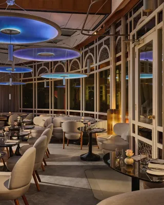 Elegant restaurant dining room with curved seating, dark tables, and large blue circular ceiling lights.
