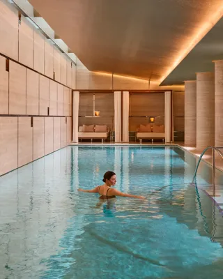 Guest swimming in a serene indoor spa pool with stone columns, warm lighting and steps with handrail.