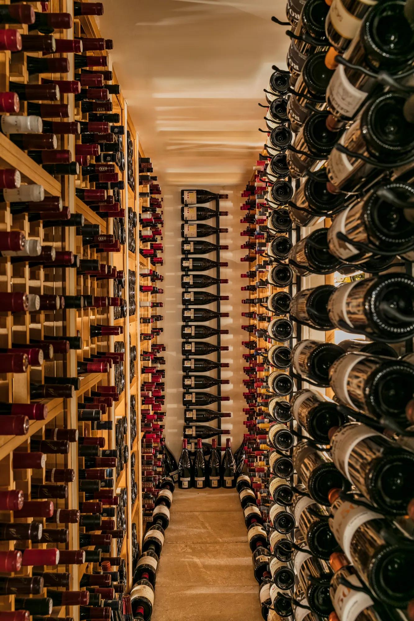 Narrow wine cellar lined with floor-to-ceiling racks filled with bottles on both sides.