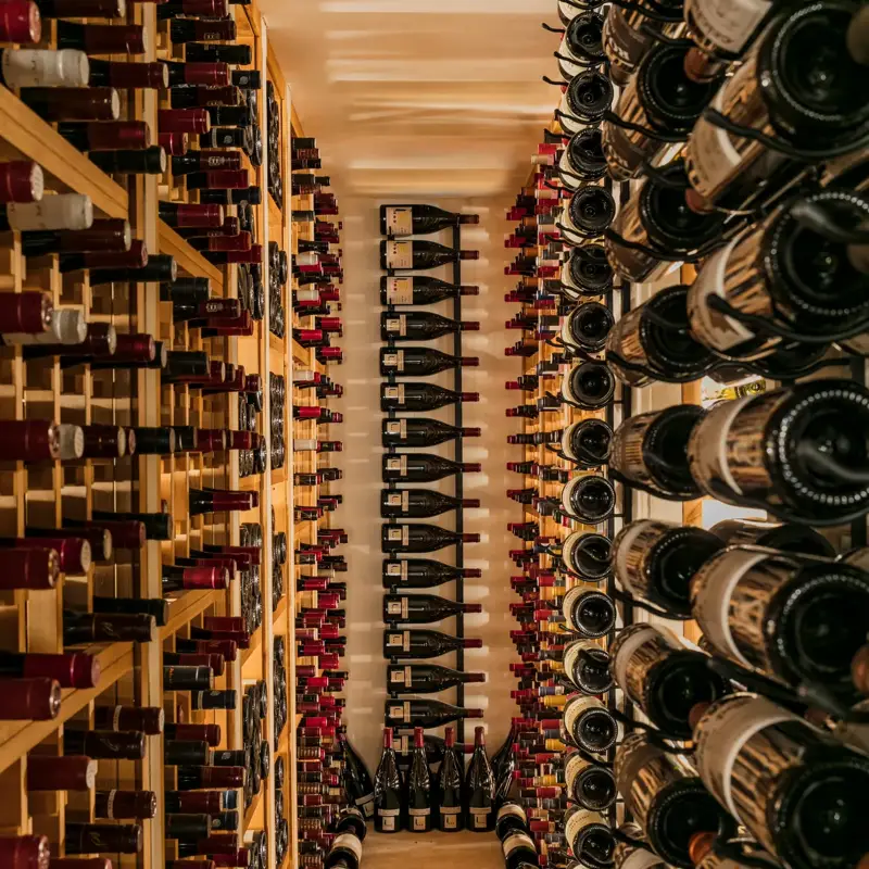 Narrow wine cellar lined with floor-to-ceiling racks filled with bottles on both sides.