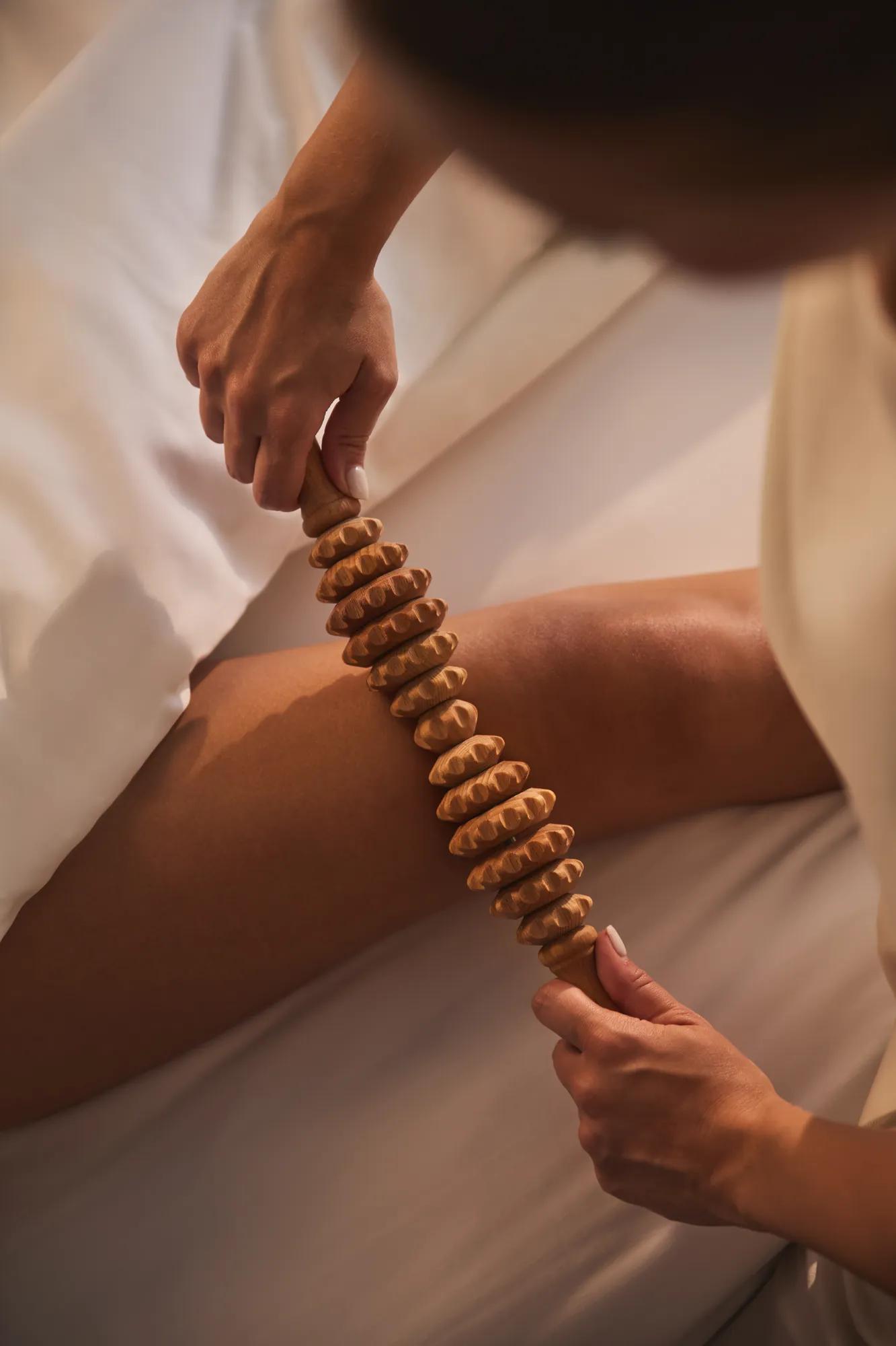 Gros plan d’une personne utilisant un rouleau de massage en bois sur sa jambe lors d’un soin spa.