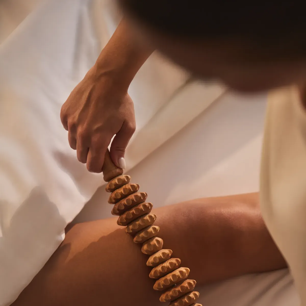 Gros plan d’une personne utilisant un rouleau de massage en bois sur sa jambe lors d’un soin spa.