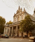 Large stone church with classical columns and dome, framed by trees and London taxis passing