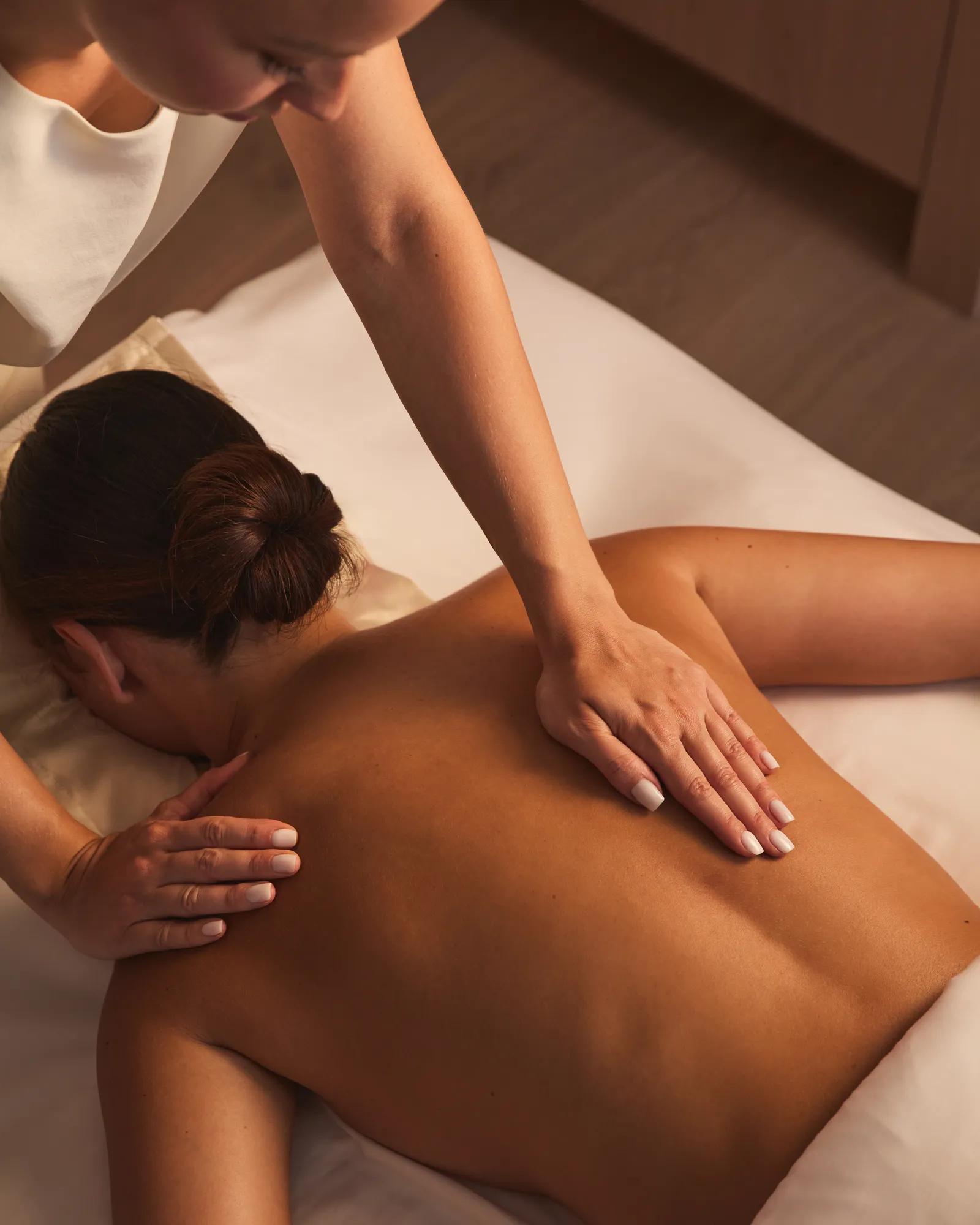 Therapist performing a back massage on a guest lying face down on a treatment bed