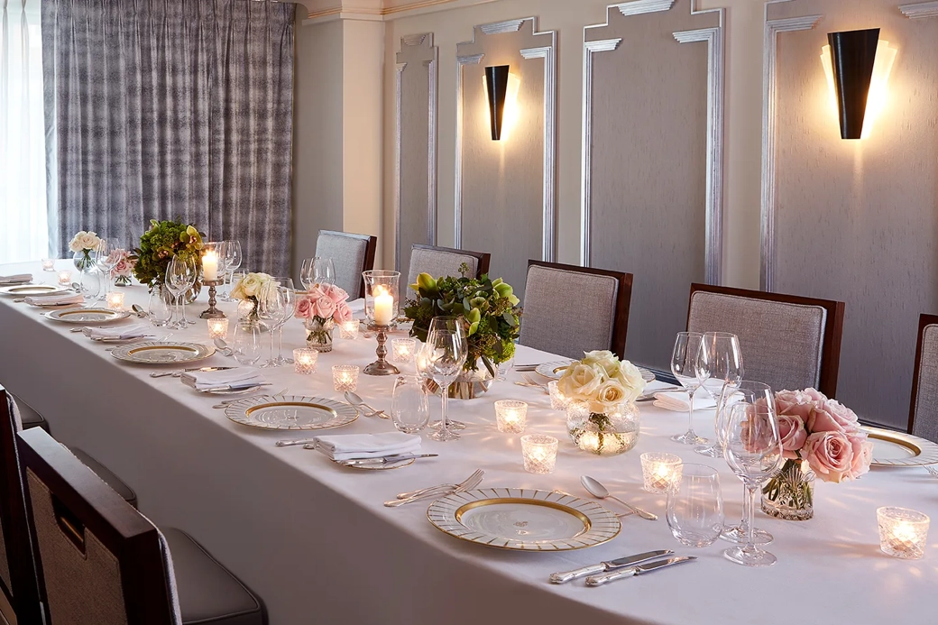 The Clarence Room at Claridge’s prepared for an intimate dinner with a long table dressed in white linen, floral arrangements, candlelight, and elegant place settings.