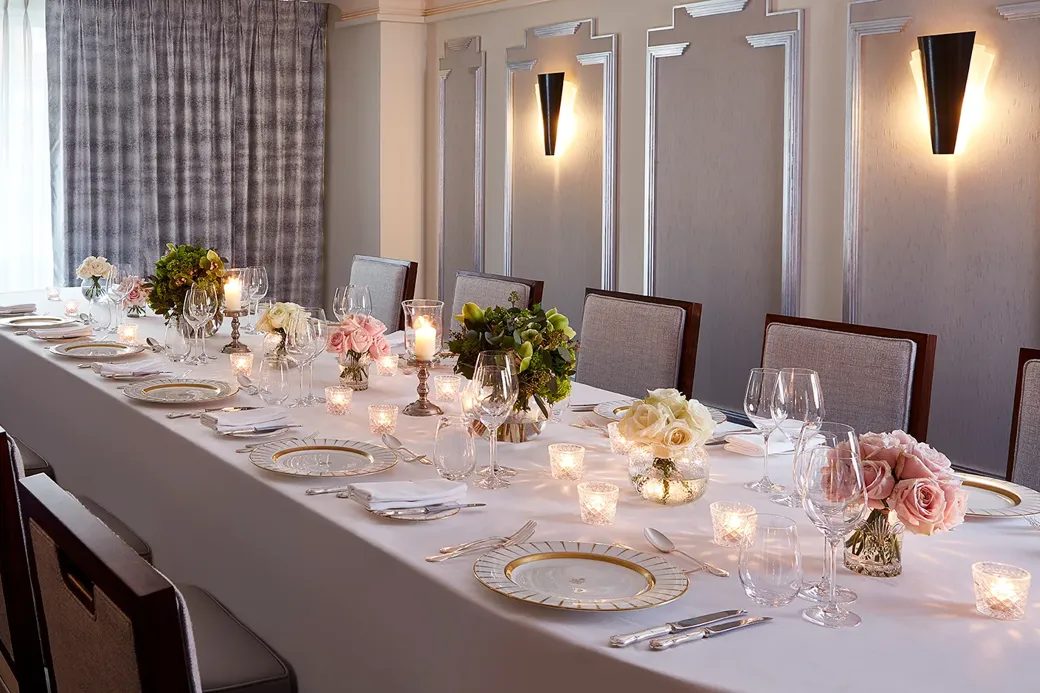 The Clarence Room at Claridge’s prepared for an intimate dinner with a long table dressed in white linen, floral arrangements, candlelight, and elegant place settings.
